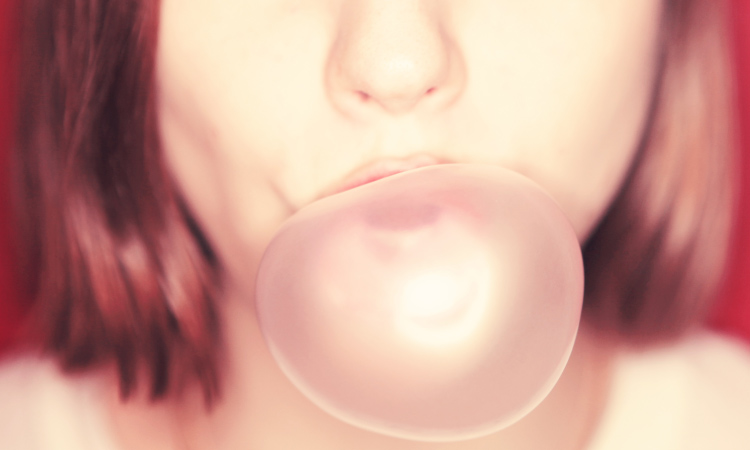Close-up of a brunette woman blowing a pink gum bubble against a red wall