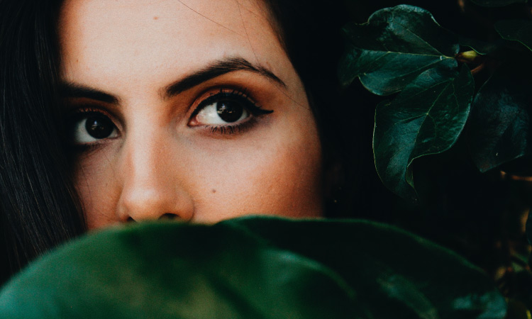 Brunette woman hides her mouth behind a green leaf due to her bad breath